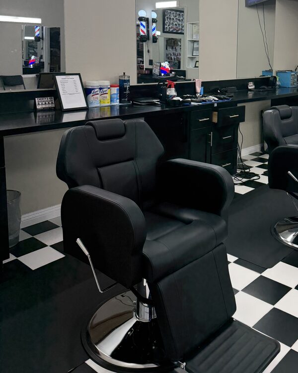 The barber chairs and the long black counter under the mirrors, on the checkered floor