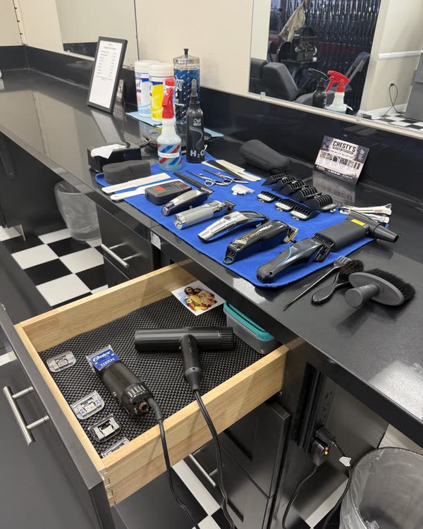 A barber station with clippers, guards, scissors and brushes laid out on a blue mat